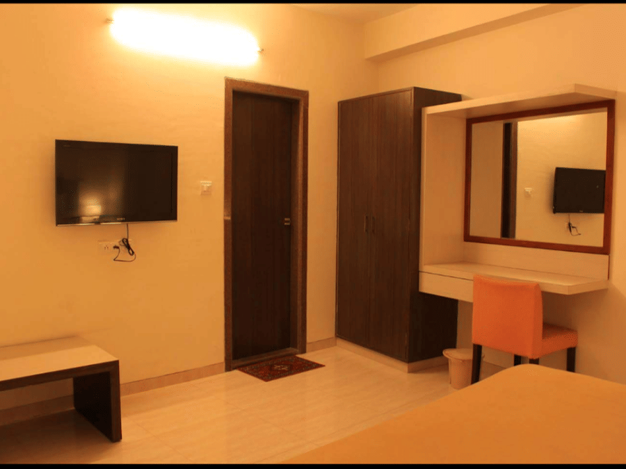 deluxe room showing a bed corner, wall-mounted television, and a dark wooden bathroom door.