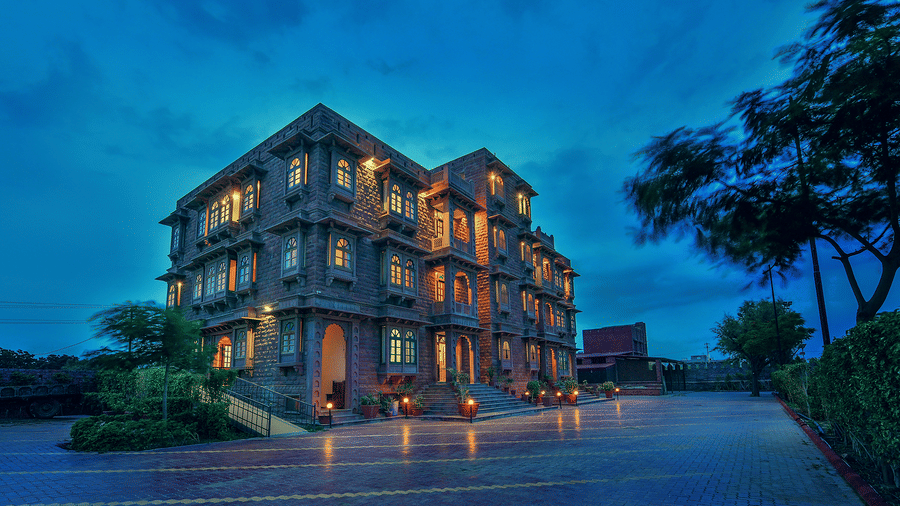A multi-storey stone building at Garh Govind, illuminated by lights along the facade and courtyard under an evening sky.