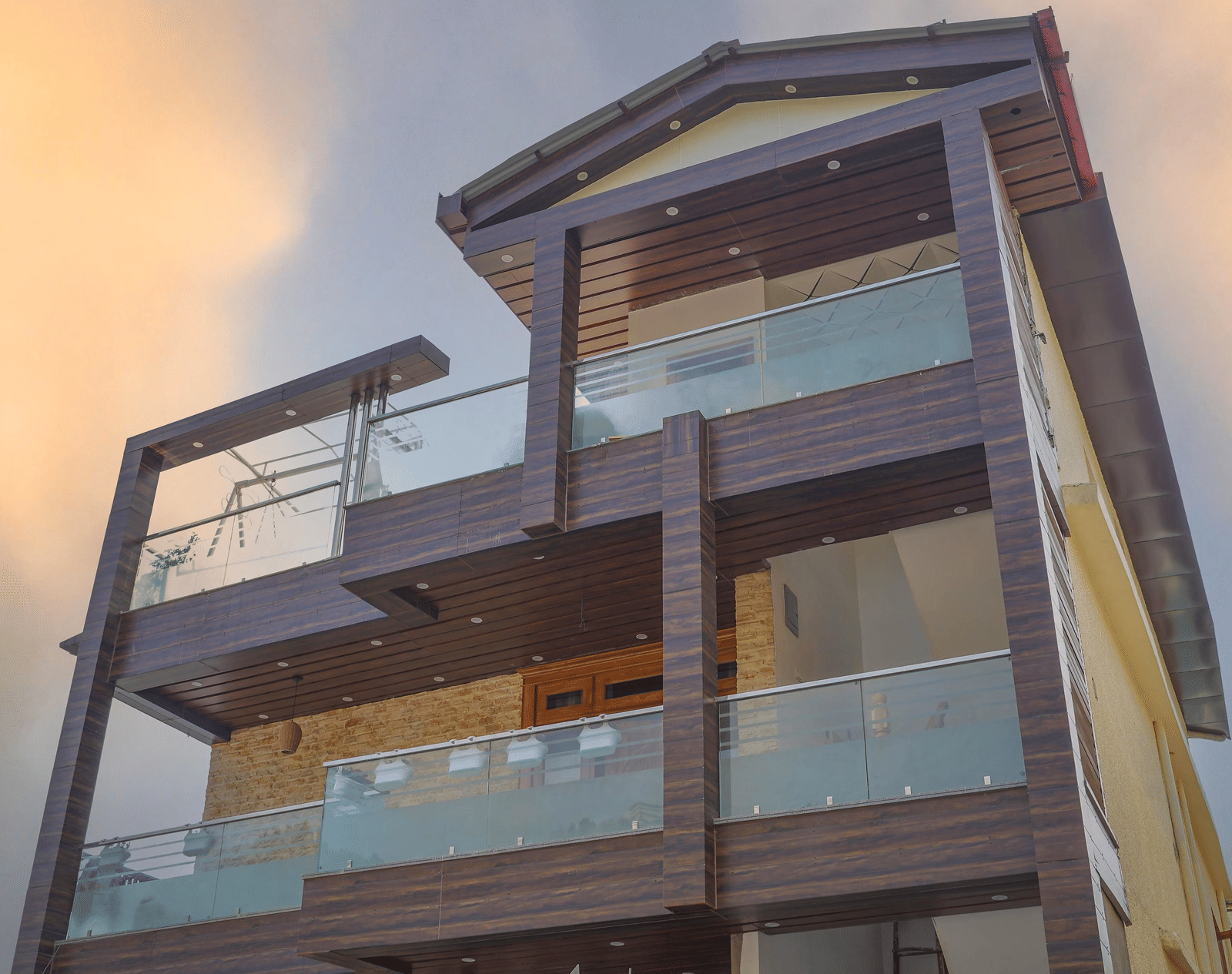 The facade of Perfectstayz Value Paradise, Mussoorie with glass balconies and wooden exterior under a cloudy sky.