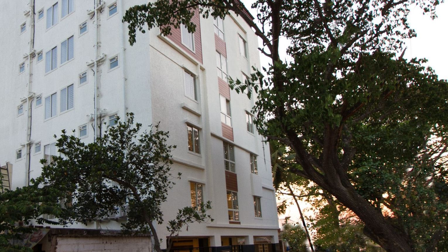 The multi-storey building of Sanctum Suites Whitefield, Bangalore amongst trees under a daytime sky.