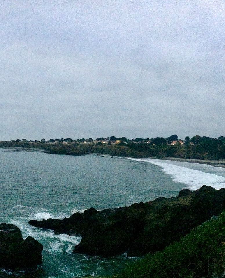 A scenic coastal view with rocky cliffs, ocean waves, and a cloudy sky in the background.