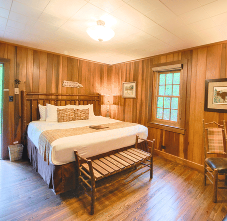 full view image of the a bedroom with a couple bed along with a small seating are in front of the bed - Historic Tapoco Lodge
