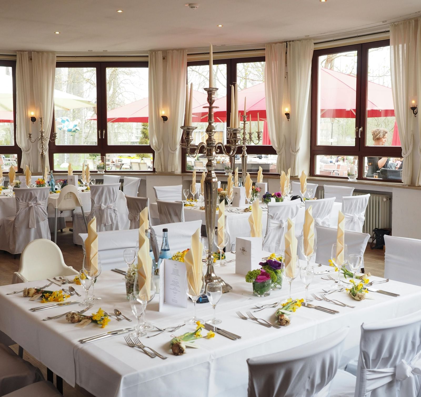 Wedding reception setup in a bright hall, long tables and chairs with cloth, and floral decorations