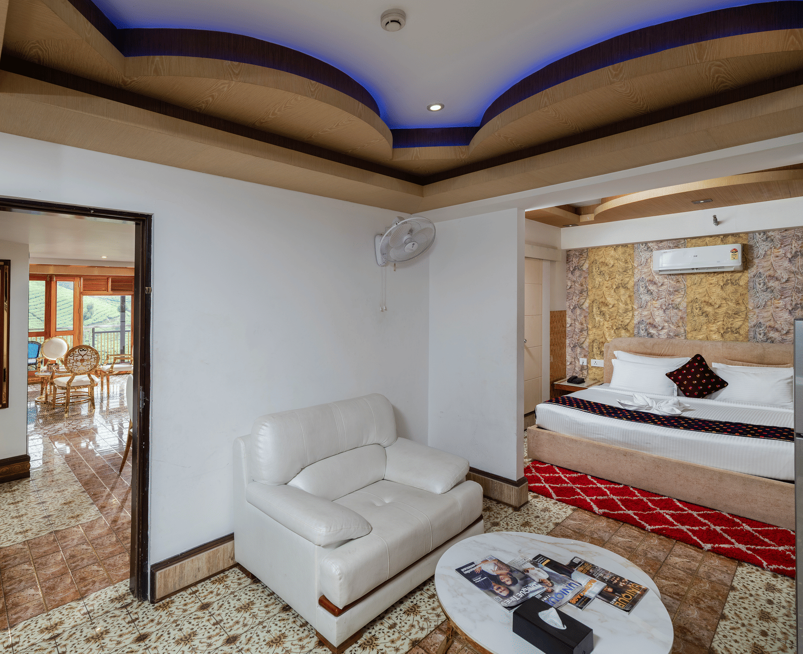 A bedroom view of the Presidential Suite at Parakkat Nature Hotel and Resorts, Munnar, featuring a large bed, luxurious seating, mirrored surfaces, and a patterned accent wall.