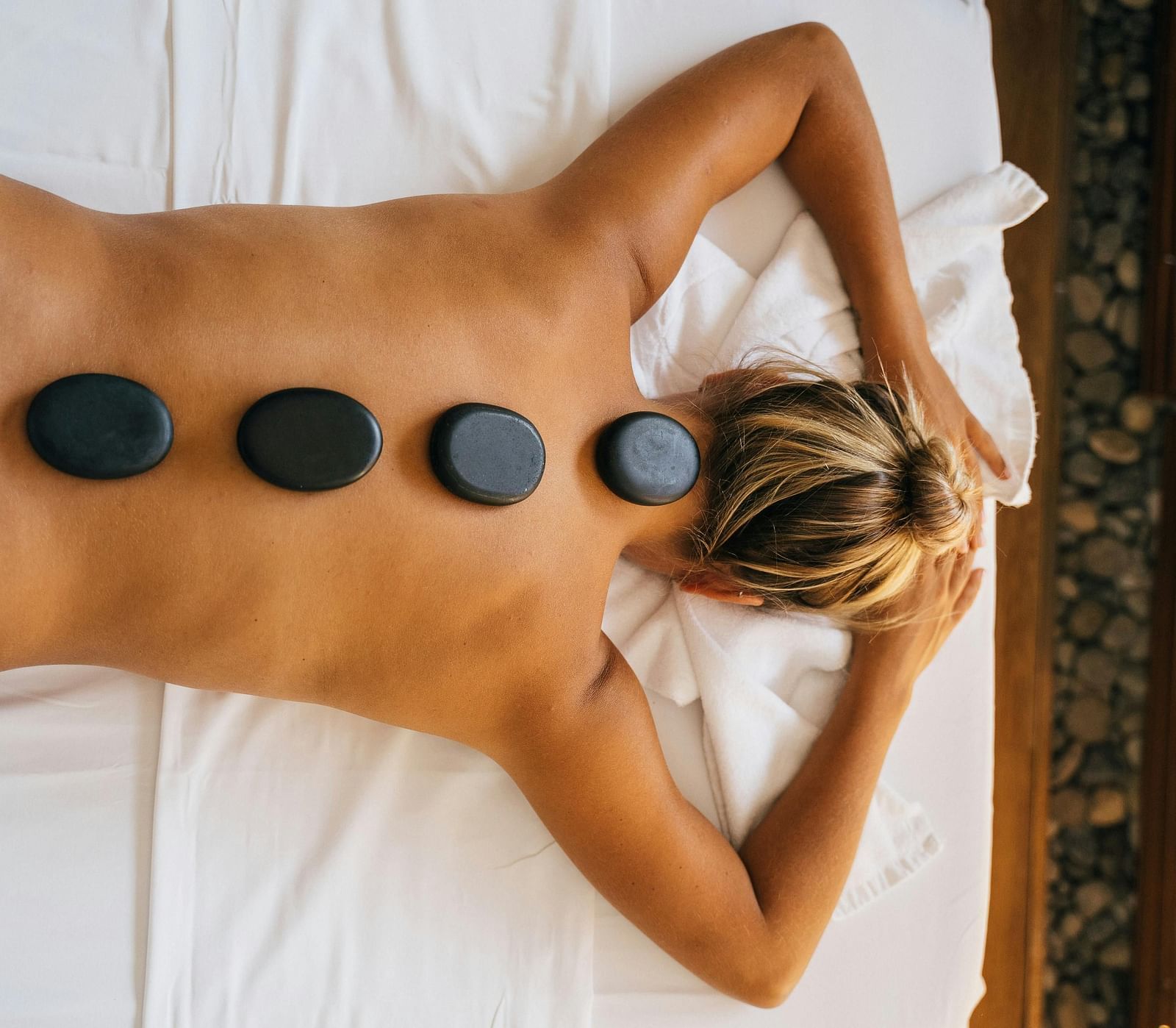 A woman lying down with back with black stones kept over her spine.