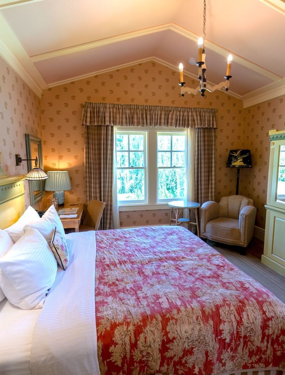 Side view of a room in Tallman Hotel, featuring plush bedding, an arched ceiling, an upholstered sofa for one, and ample natural lighting entering from the open glass windows.