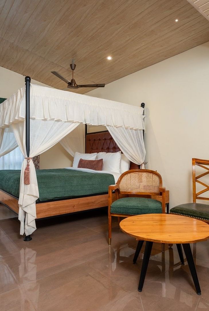 Premium Room featuring a large bed with curtains neatly tied to rods on all four sides, also includes chairs and tables arranged neatly.