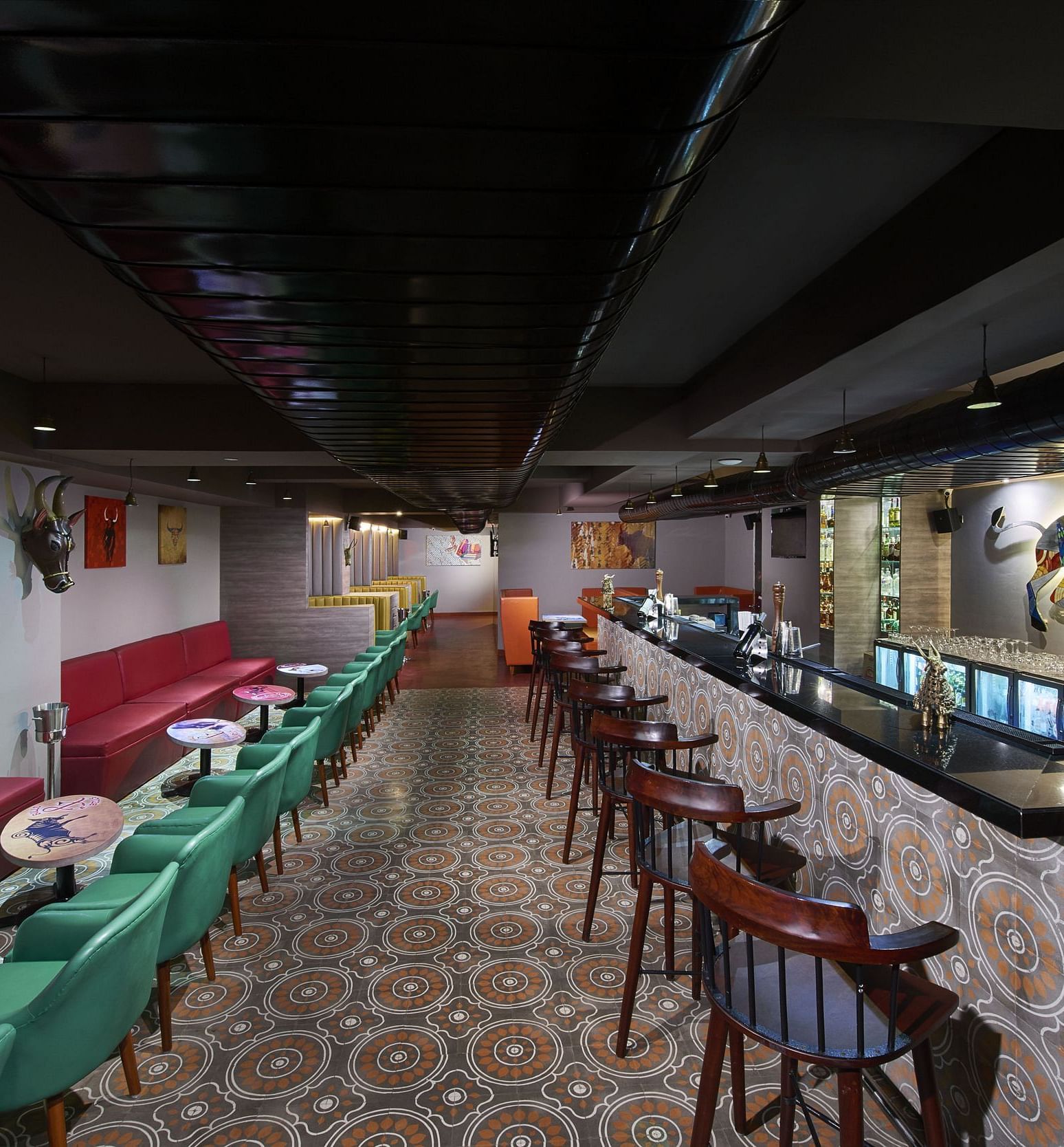 A brightly lit bar with red couches, a long bar counter, and a colorful wall mural | Regency Tirunelveli By GRT Hotels
