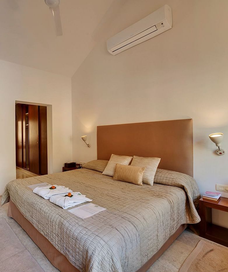 A wide angle image of a bedroom featuring a king size bed and a seating area with a cosy sofa - Shreyas Retreat