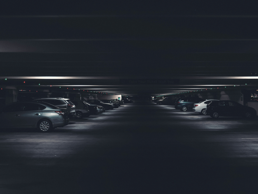 Dimly lit underground parking garage with cars lined on both sides and overhead indicator lights.