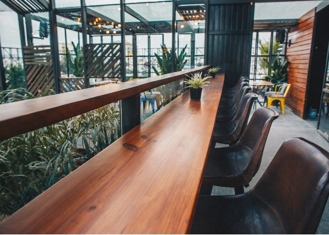 A wooden counter top on a higher level overlooking green plans with maroon leather chairs lined in front of it.