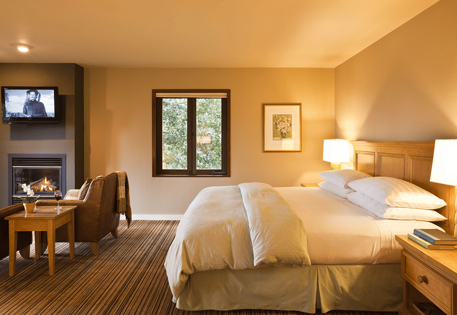 A cozy guest room with a large bed, fireplace, and window with a view of trees.