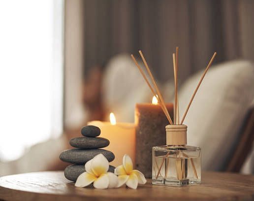 Relaxing spa-like scene with candles, diffuser, stones, and flowers.