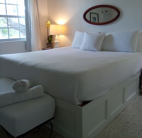 Bed at Casa Morada with white linens, towels on a bench at the foot, and a window with curtains in the background.