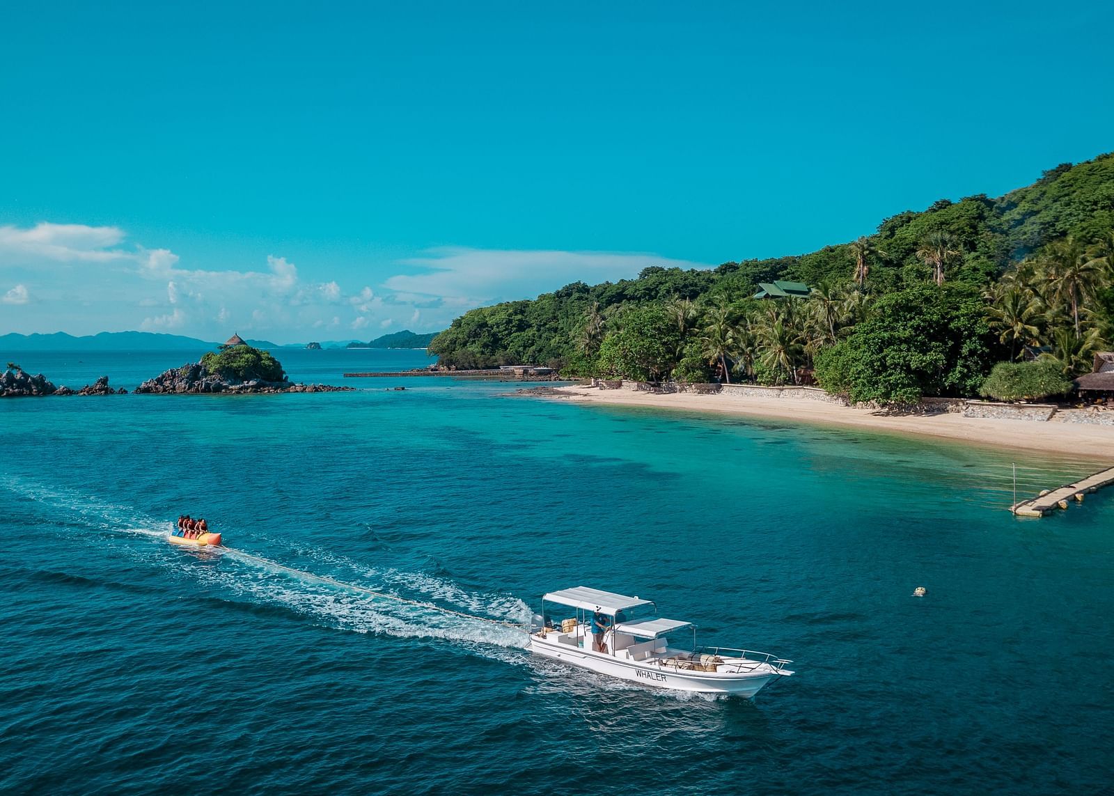 Speedboats on turquoise water near sandy beach and green hills at Flower Island Resort.