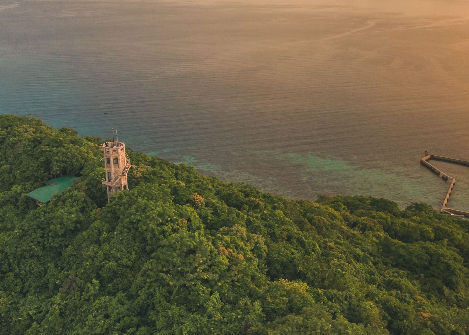 Aerial view of a green hill with a white tower and sea in the background at Flower Island Resort.