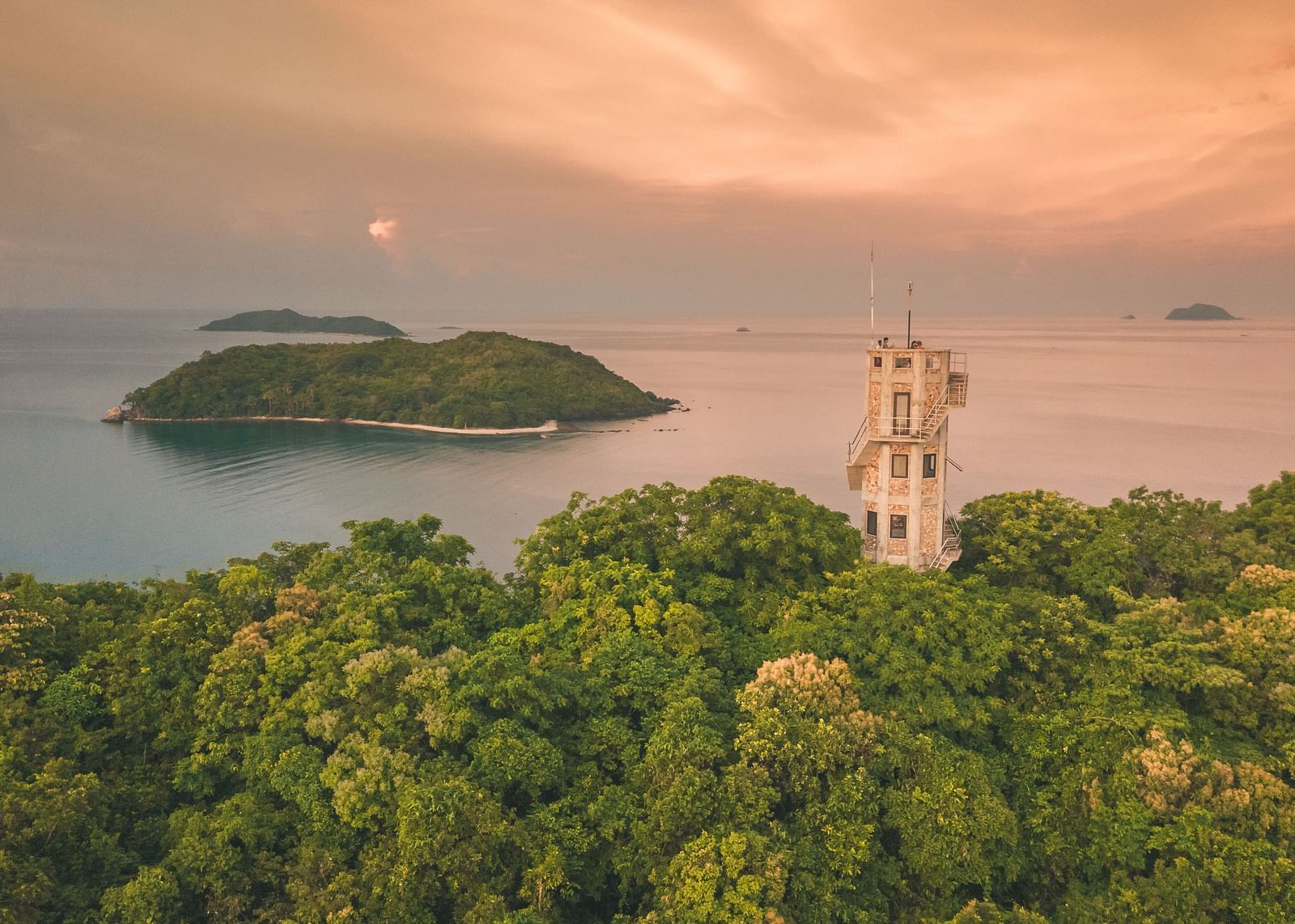 Aerial view of a green island with a white tower structure near Flower Island Resort.