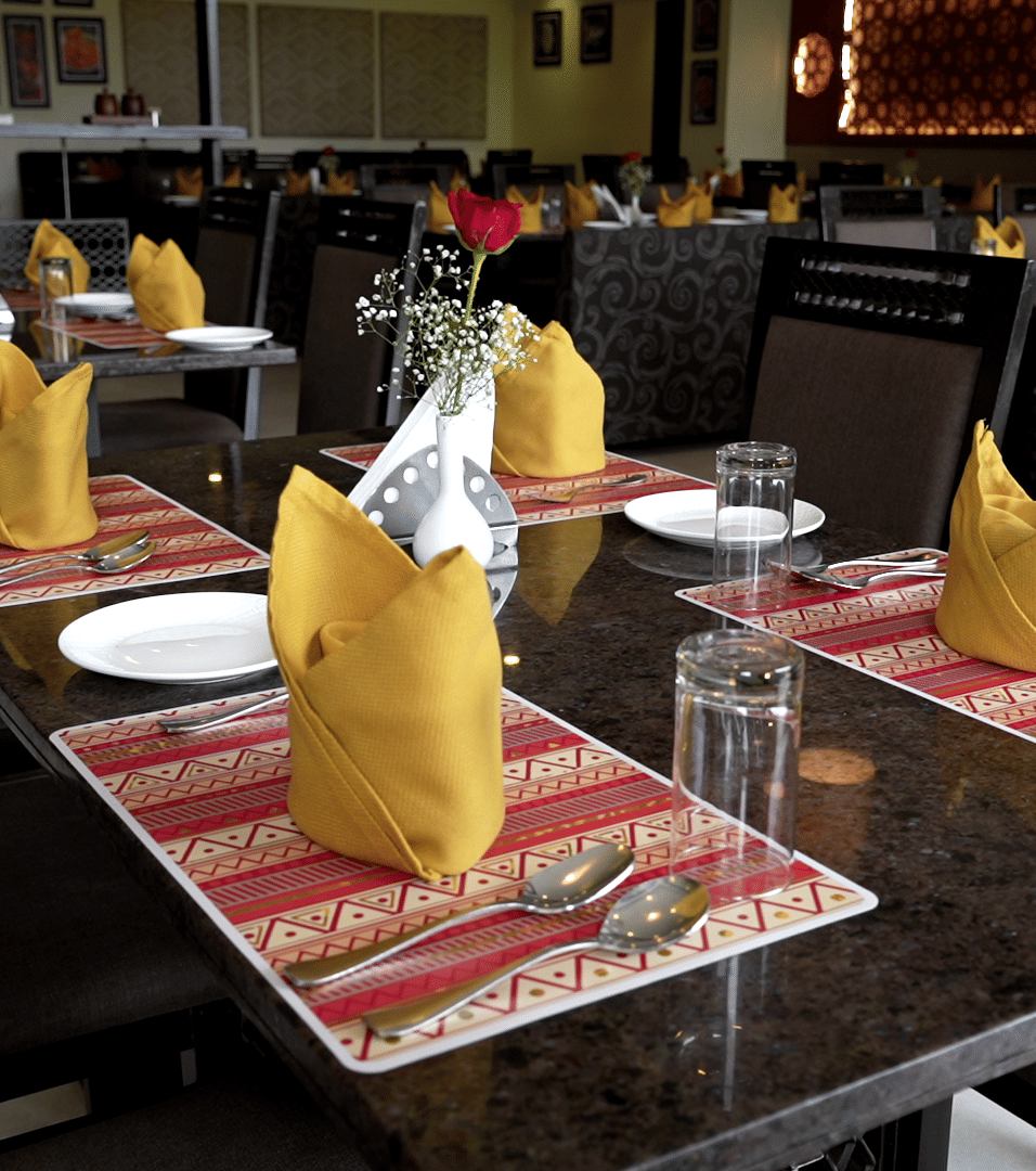 Close-up of a dining table set with folded napkins, cutlery, and tableware - Narayani Heights Hotel & Resorts