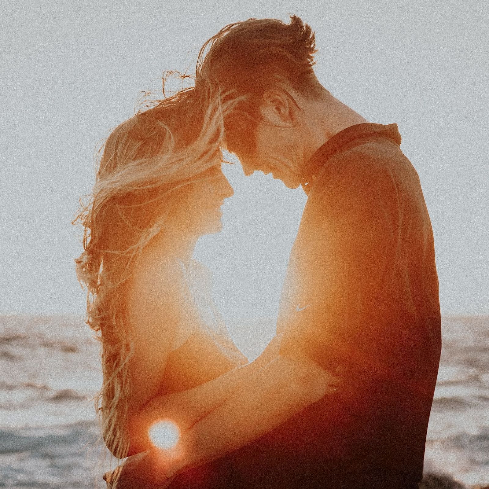 Image of a man and a woman holding each other with a waterbody in the background.