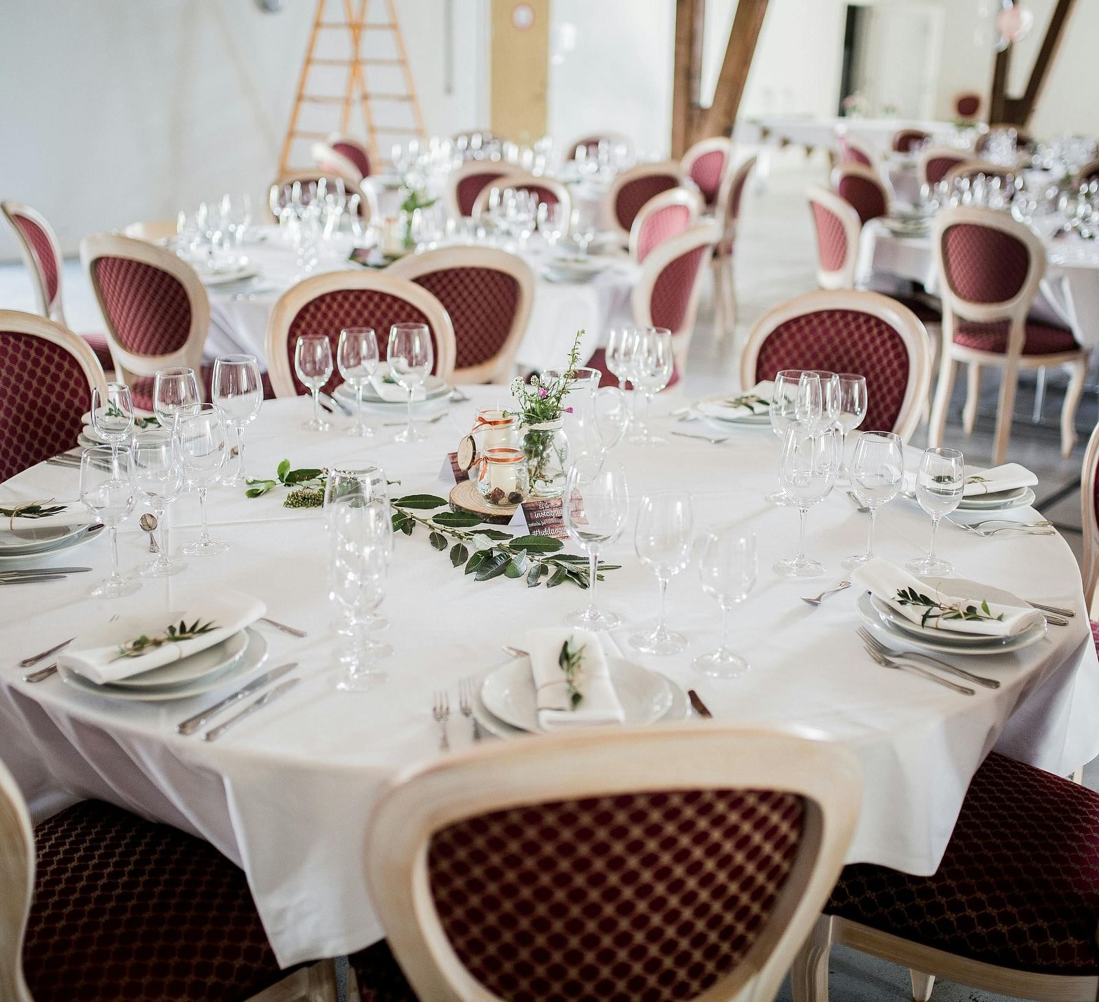 image of a round shaped table covered with a white cloth in a banquet hall with maroon coloured cushioned chairs surrounding the table