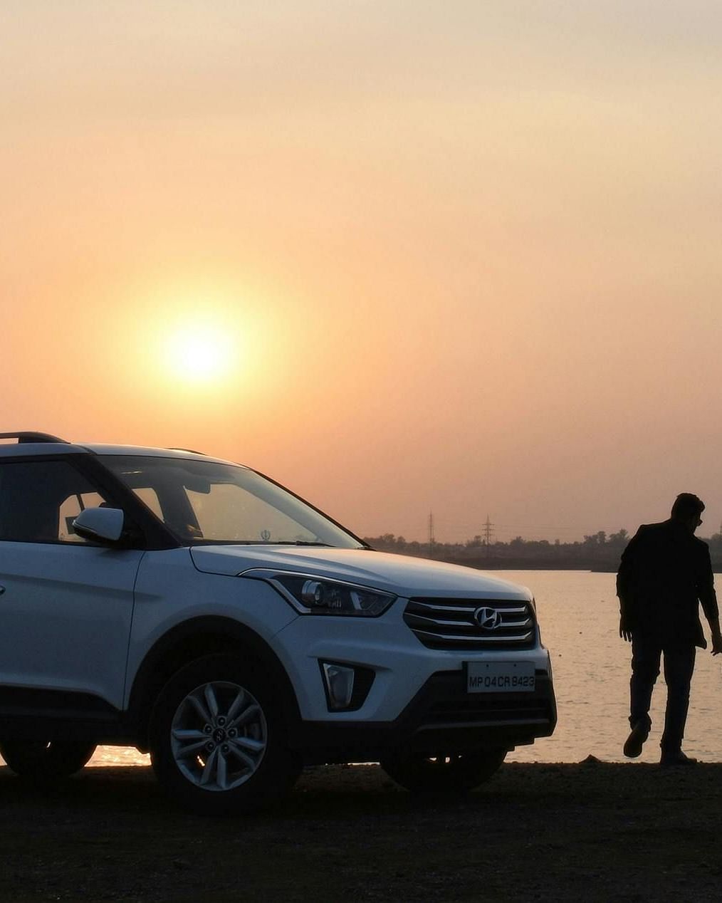 Silhouette of an adult and child holding hands beside a car, gazing at the lake.