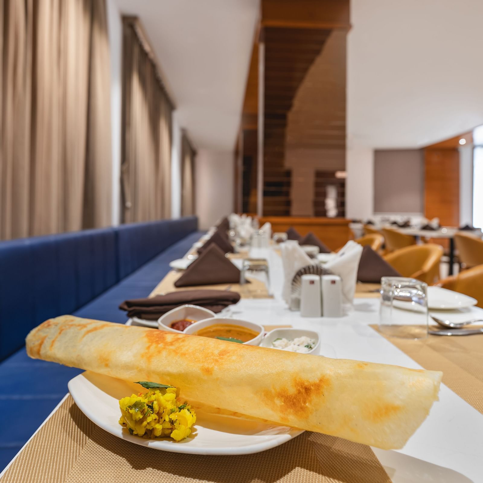 A long, thin crepe with a side of filling sits on a plate on a set table in a restaurant - Lords Eco Inn Ambaji.