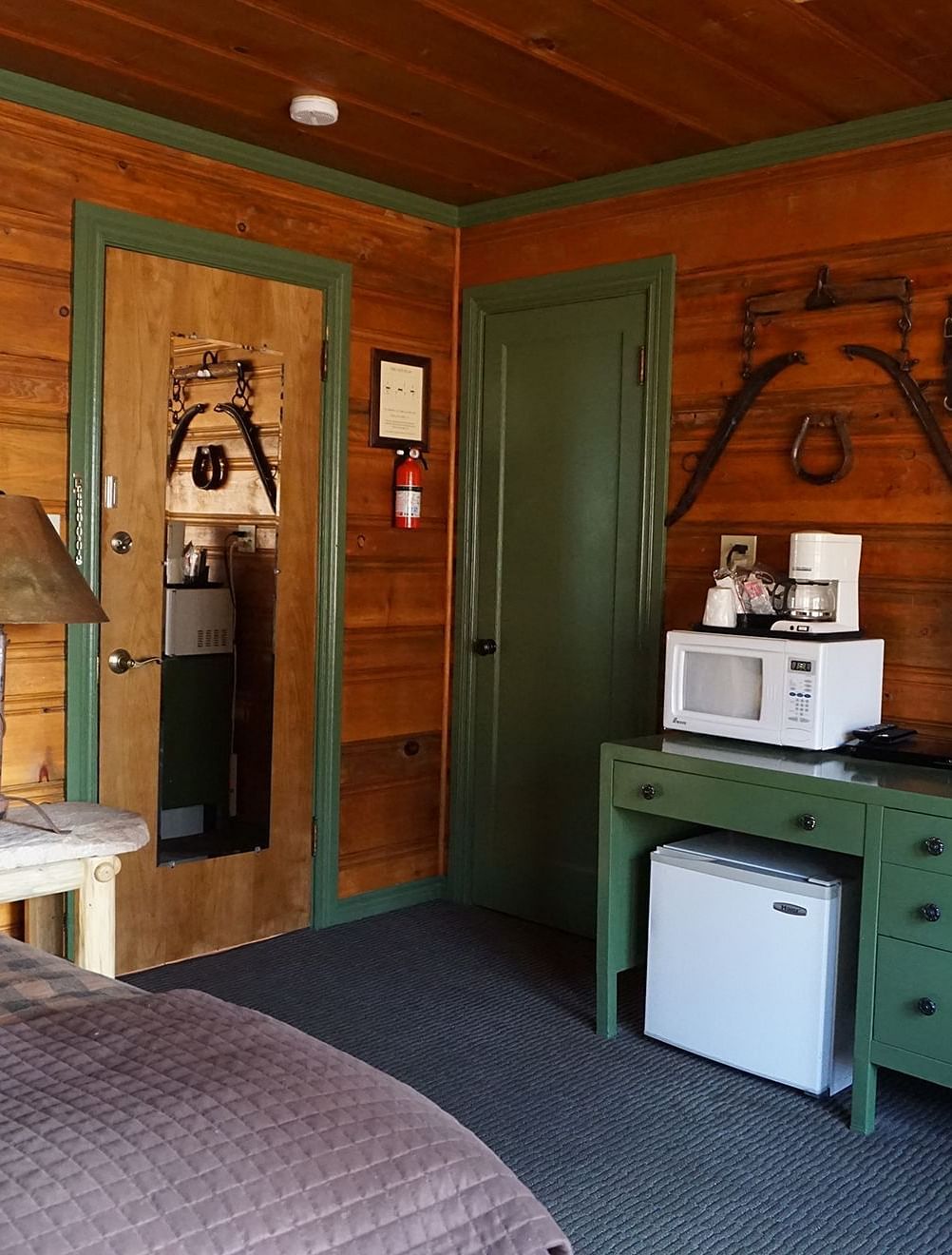 A room at Shaver Lake Village Hotel with a double bed, a lamp on a night stand, a green cabinet and wooden paneling throughout.