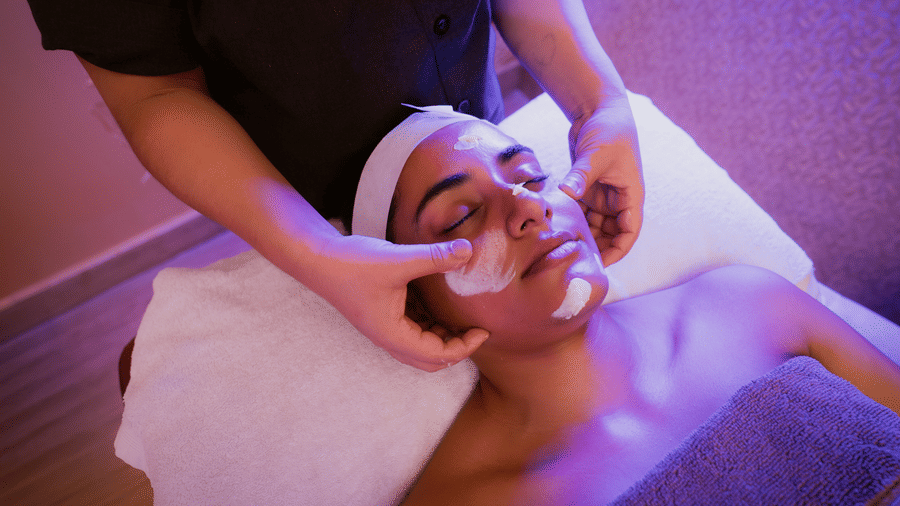 Therapist applying cream to a guest's face during a facial, with a white headband and towels in place, at Hasta Spa, Ilara Hotels & Spa, Tada.