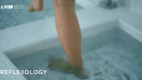 Person stepping into a soothing water pool for a reflexology session, promoting relaxation and therapeutic foot care in a spa setting at YO1 Longevity & Health Resorts