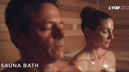 2 individuals relaxing in a sauna bath, both with closed eyes and glistening skin from the heat at YO1 Longevity & Health Resorts