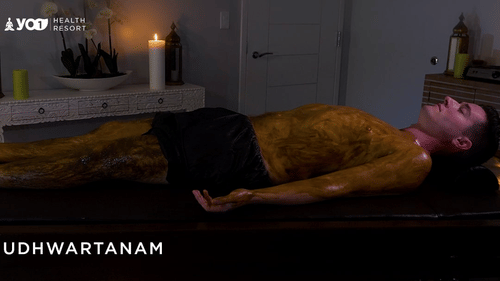 A man lies covered in herbal paste during Udwartanam, an Ayurvedic treatment that exfoliates, detoxifies, and stimulates metabolism through dry powder massage at YO1 Longevity & Health Resorts