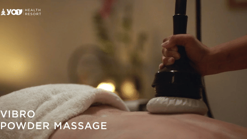 A person lying on their back and receiving back massage with a vibro powder device by a therapist's hand at YO1 Longevity & Health Resorts