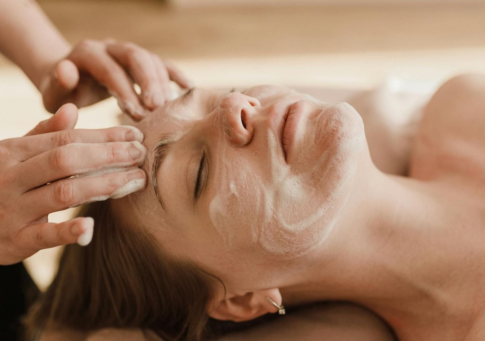 A lady relaxing with her head on a spa table while someone gently cleanses her face