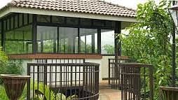 A modern house with large windows and a balcony, surrounded by greenery.