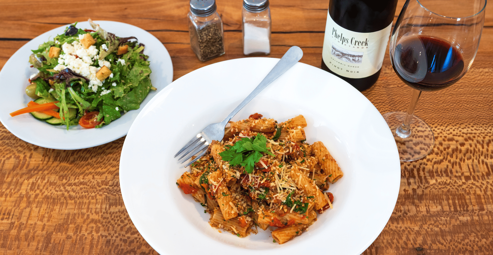 Pasta dish paired with salad and red wine served on a wooden table at The Groveland Hotel.