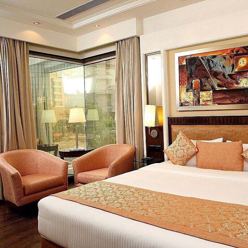 Executive Room with a double bed, bedside table with a lamp on top, cushioned seating with a table in front, and a window behind at Inde Signature Tower, Gurgaon