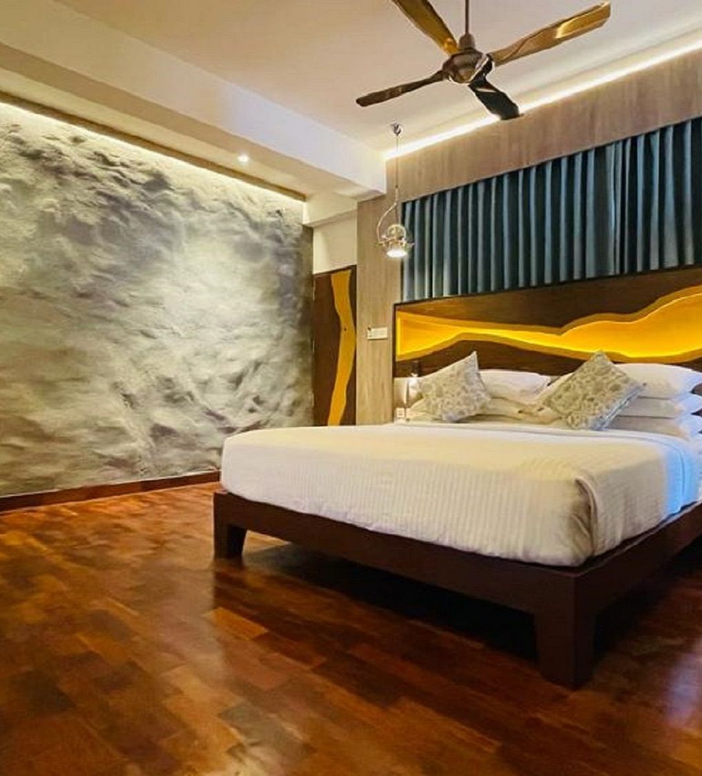 An image of timber Lodge room with a king size bed, ceiling fan, decorative items, and wall paintings - GReaT trails Kodaikanal by GRT Hotels