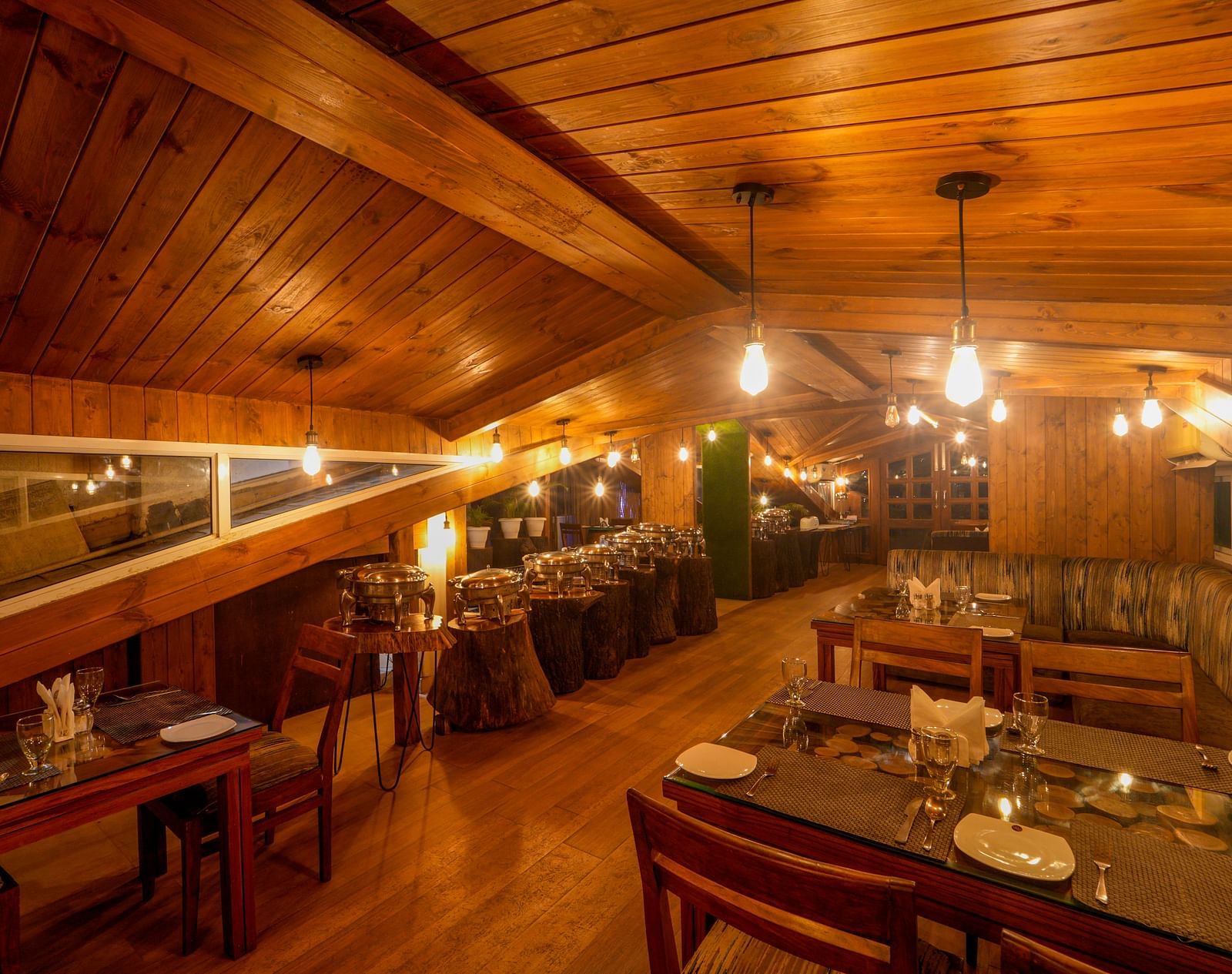 The wooden interiors of the restaurant at DLS Whispering Winds with chairs and tables which it lit with bright lighting