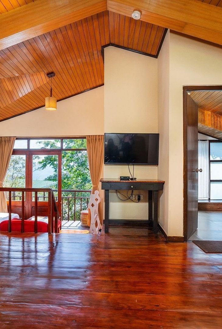 Chalet room with a spacious bed, large windows with nature views, wall-mounted television, table with chair, and attached bathroom at Summit Norling Resort & Spa, Gangtok