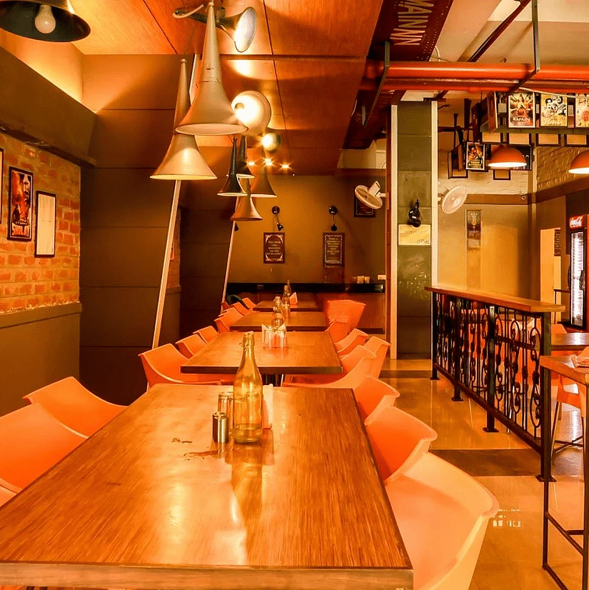 An image of a restaurant with several chairs and tables, ceiling lights hanging, photo frames on the walls, and other things - Max Hotel Jabalpur