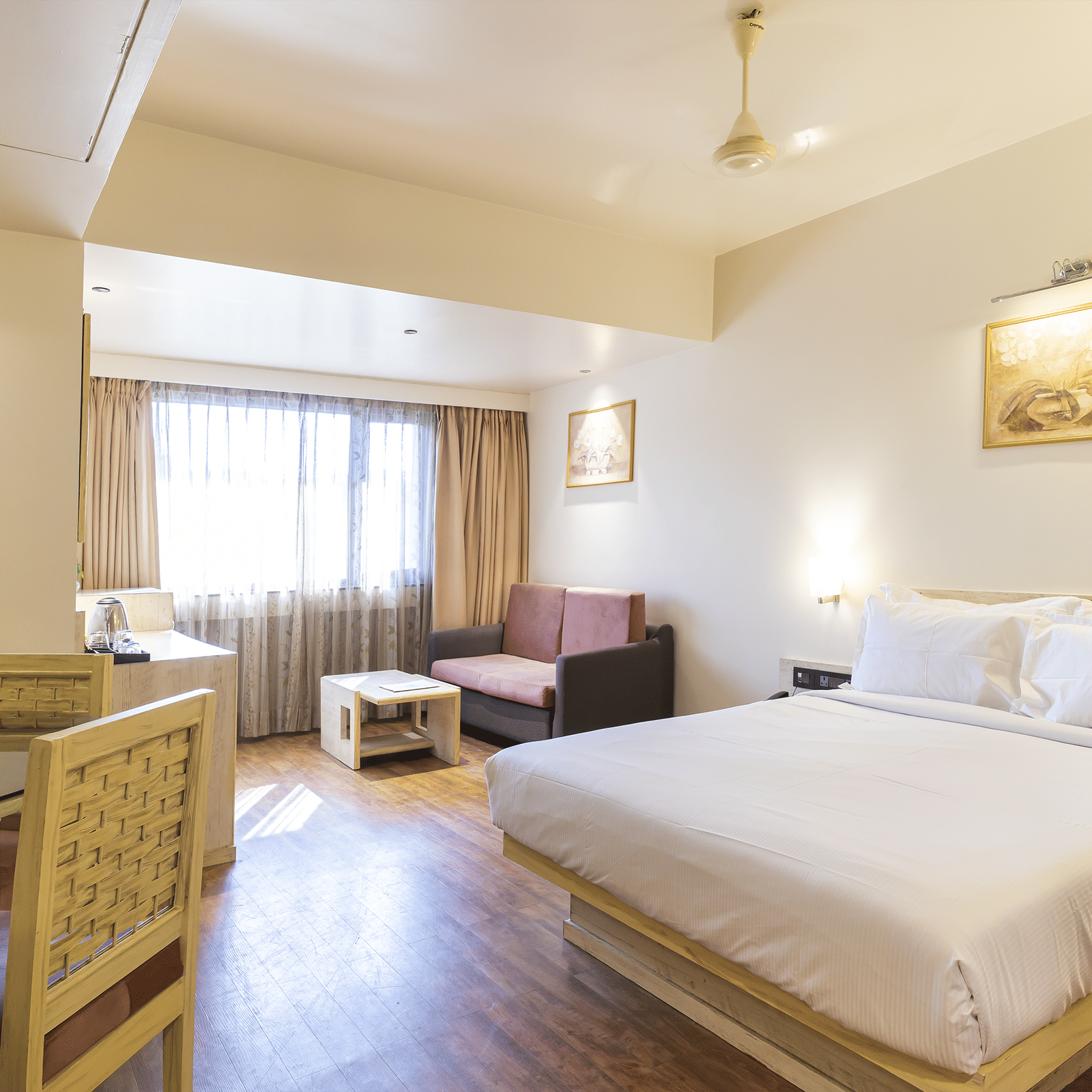 Bedroom with a king size bed, dining table & chairs, a seating space by the window and painting on the wall at Infiniti Hotel, Indore.