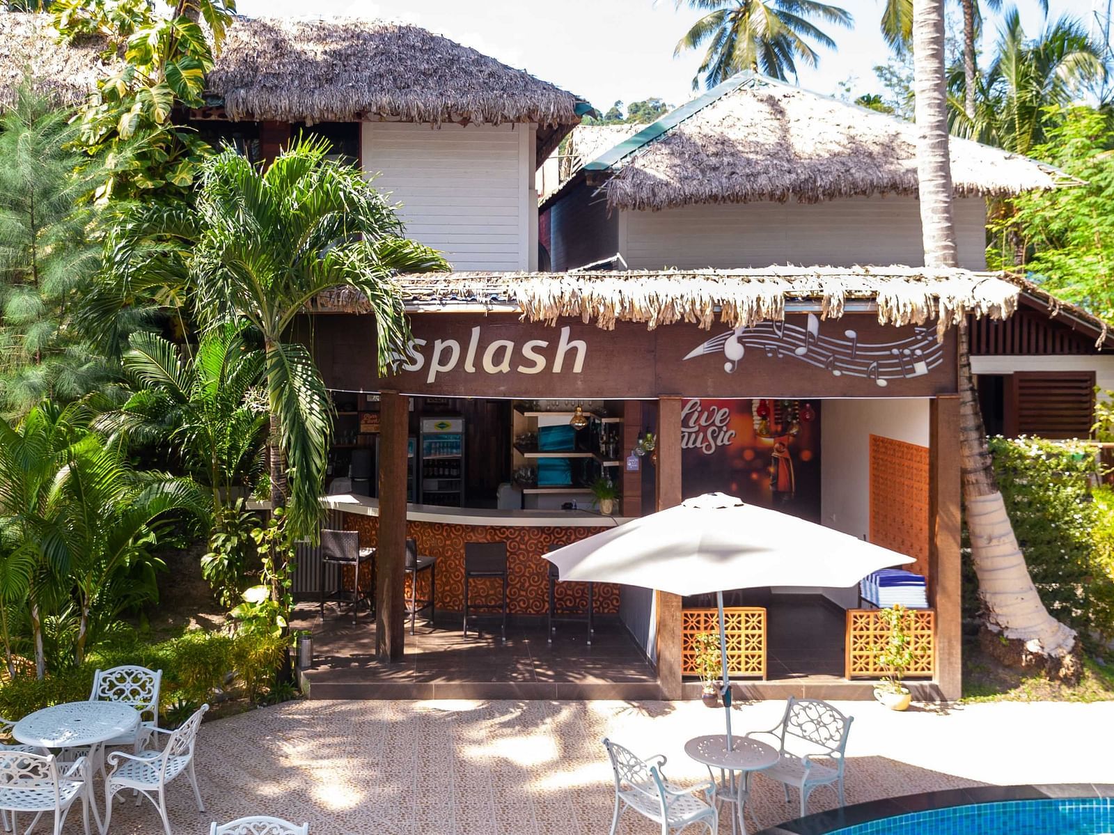 Splash Pool Bar at Coral Reef Resort & Spa in Havelock featuring wooden facade with a sign reading  Splash located near a pool area. The surroundings feature tropical plants and a relaxing outdoor seating area - Coral Reef Resort & Spa, Havelock