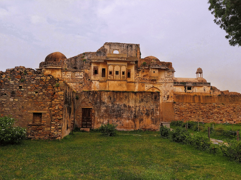 Walls and bastions of Chittorgarh Fort rising over grassy grounds, with rugged stone surfaces and elevated structures reflecting defensive strength and historic settlement layout