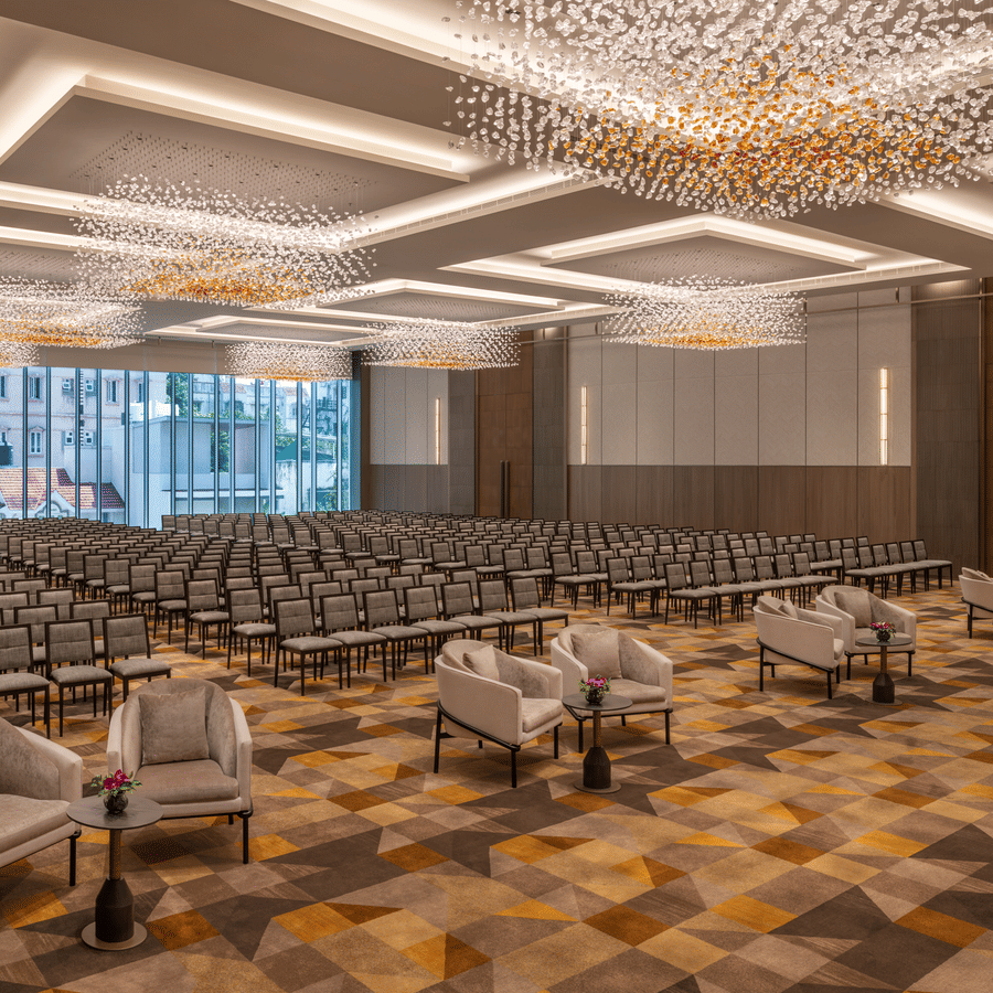 The grand banquet hall of Ballroom 1 arranged in theatre seating with plush armchairs in the front row and crystal chandeliers above at The Residency Towers Chennai.