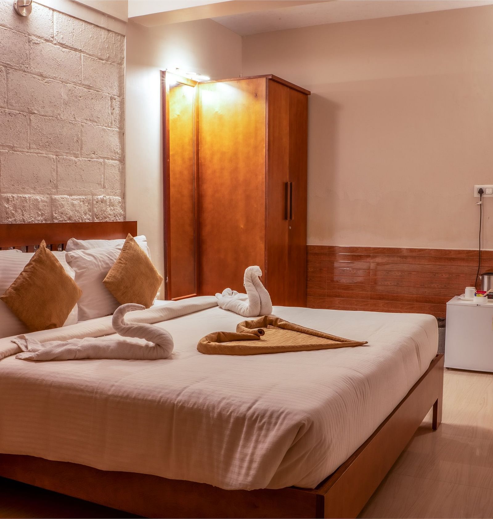 Standard Room showcases a neatly made bed with white linens and decorative brown towels, with two pillows and a small square cushion | Woodstock Resorts, Coorg