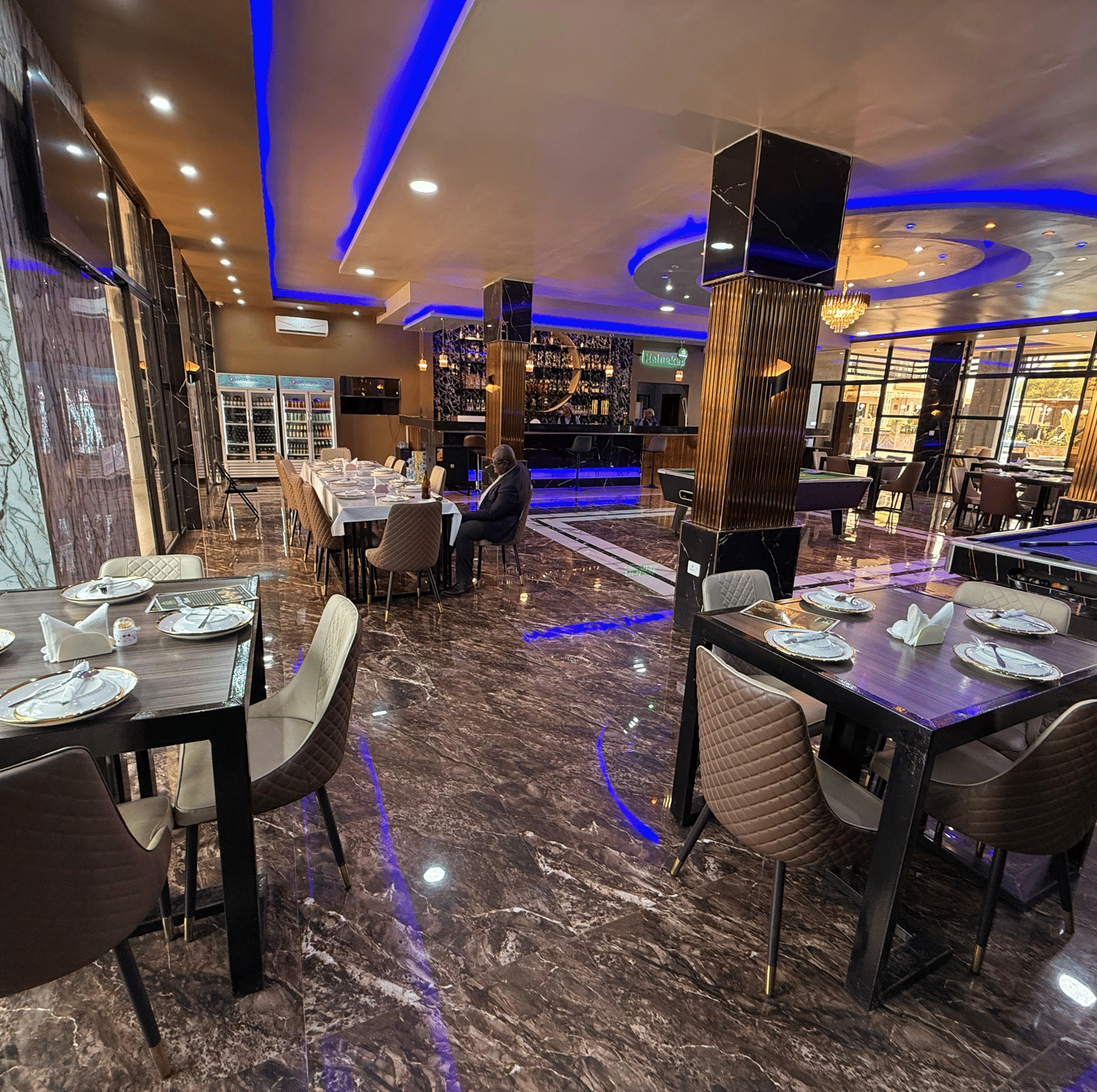 A lavish indoor dining area with marble-effect flooring, dark tables, place settings, and striking blue neon lighting at Luffu Club.