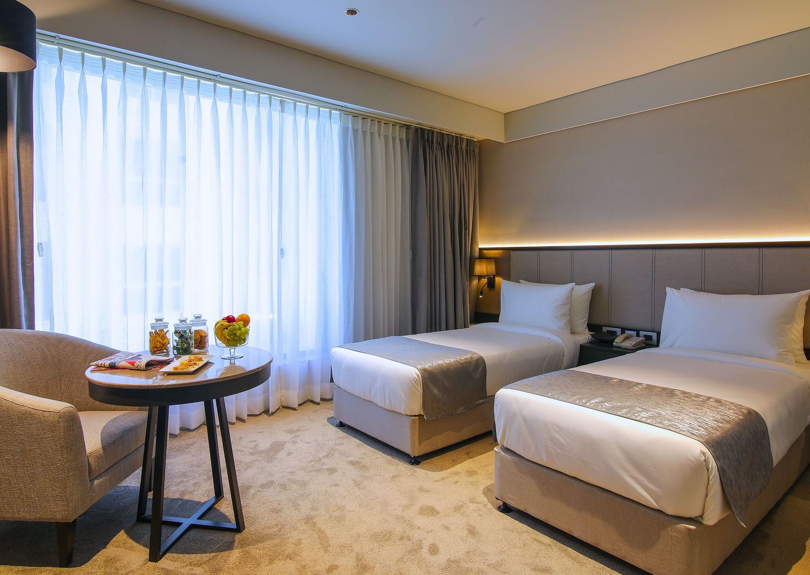 Twin beds with a chair and table in front of it inside one of the rooms - Essentia Premiere, Pune