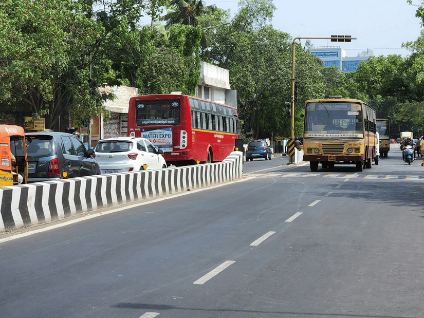 An overview of a road in Chennai with traffic on one side and a bus on the other side, with trees on either side of the road.