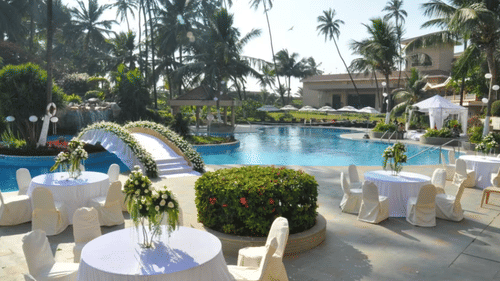 A poolside dining area with tables and chairs beside a swimming pool surrounded by palm trees at The Retreat Hotel and Convention Centre.