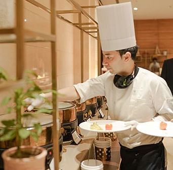 A chef grabbing food from a buffet while holding two dishes at Nirvana Luxury Hotel, Ludhiana.